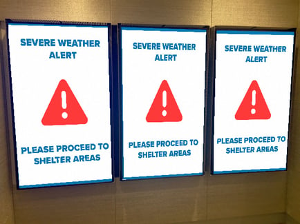 Three displays of digital signage displaying message of severe weather alert please proceed to shelter areas