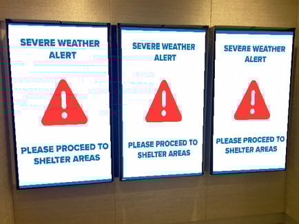 Three displays of digital signage displaying message of severe weather alert please proceed to shelter areas